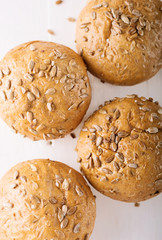 Four buns with seeds on a light wooden background, top view 