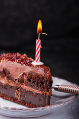 Piece of chocolate cake with candle on a dark background.