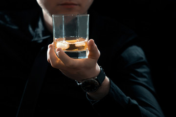 Closeup man in black with glass of whiskey and ice in dark room