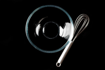 Glass transparent bowl with metal whisker aside on black background directly from above with reflection