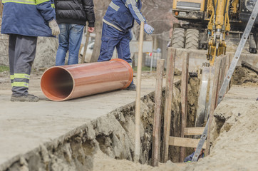 Placement sewerage  pipe at the street with workers and bagger in background