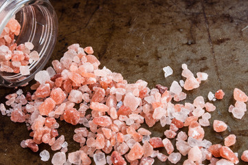 Scattered Himalayan pink salt crystals from glass bottle on rusty metal background