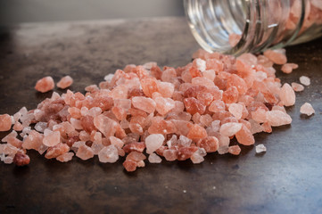 Scattered Himalayan pink salt crystals from glass bottle on rusty metal background
