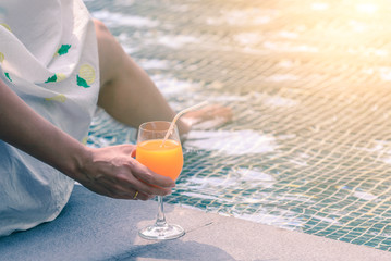 Rear view of beautiful woman in hat is holding orange juice glass in summer.