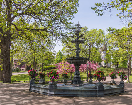 Ornate antique fountain surrounded by green trees and spring flowers on a sunny day in Irvine Park in Saint Paul, Minnesota.