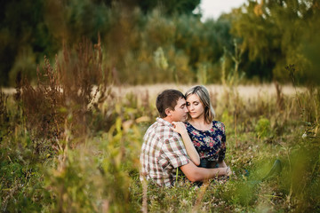 Lovers boy and girl sit arm in arm among the vegetation in the evening