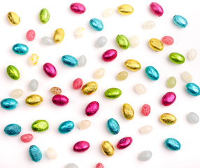 Top down view of brightly covered mini chocolate eggs and jelly beans on a white background