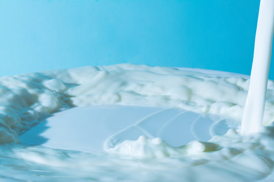 splash of milk, pouring jet stream of milk on a light blue background
