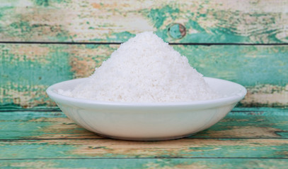 Dried coconut powder in white bowl over wooden background