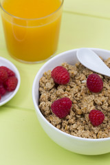 Granola in a bowl with raspberries and orange juice, muesli