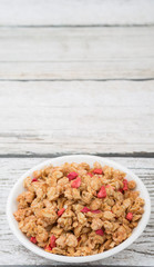 Breakfast cereal with dried raspberry fruit pieces in white bowl over wooden background
