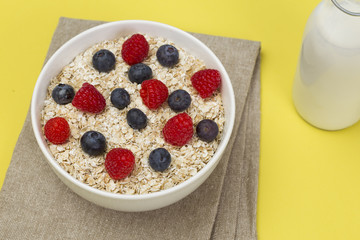 Rolled oats (oat flakes) in a bowl with raspberries, blueberries