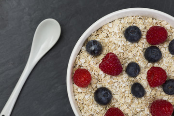 Rolled oats (oat flakes) in a bowl with raspberries, blueberries
