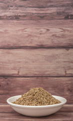 Dill herb seeds in white bowl over wooden background