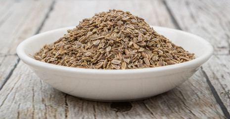 Dill herb seeds in white bowl over wooden background