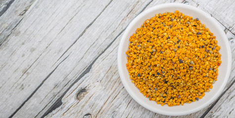 Bee pollen in white bowl over wooden background