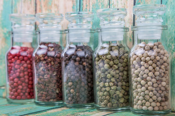 Szechuan peppercorns, green peppercorns, white peppercorns, black peppercorns and pink peppercorns in glass vial over wooden background