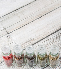 Szechuan peppercorns, green peppercorns, white peppercorns, black peppercorns and pink peppercorns in glass vial over wooden background