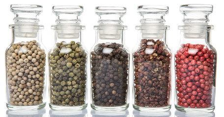Szechuan peppercorns, green peppercorns, white peppercorns, black peppercorns and pink peppercorns in glass vial over white background