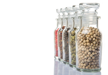 Szechuan peppercorns, green peppercorns, white peppercorns, black peppercorns and pink peppercorns in glass vial over white background