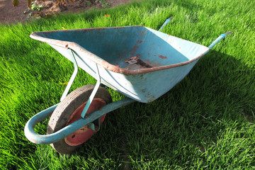 Old rusty one-wheeled wheelbarrow on the fresh lawn in the autumn garden
