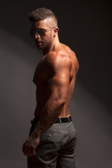 shirtless muscular man in pants and sunglasses posing in studio