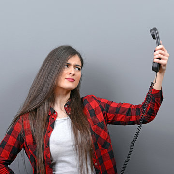 Portrait of woman having unpleasant phone calll against gray bac