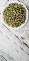 Dried green peppercorn in white bowl over wooden background