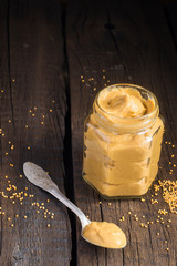 Fresh mustard sauce in a jar and mustard seeds scattered on the 