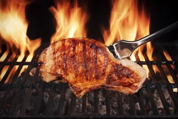 Poster Im Rahmen Schweinesteak auf heißem flammenden Barbecue-Grill mit Gabel © Alex