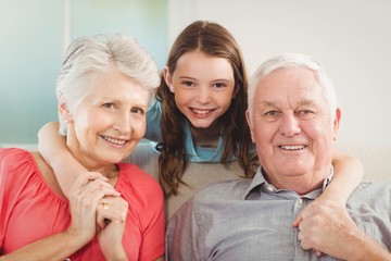 Smiling granddaughter embracing her grandparents in living room
