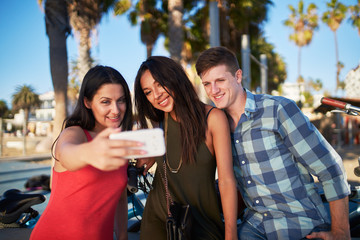 friends taking selfies under the shade of palm trees at santa monica beach