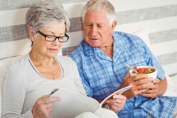 Senior couple reading magazine in bedroom