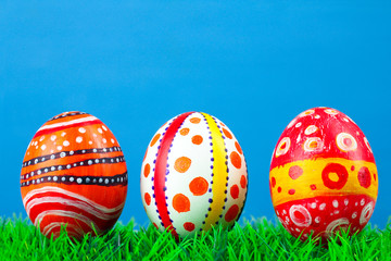 Easter eggs in beautiful and different colors lie on the grass on a blue wooden background