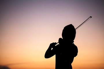 The silhouette girl playing the violin in the sunset
