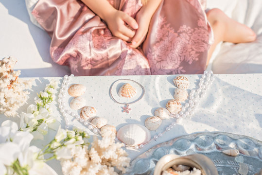 A girl in a pink dress collects seashells and corals on the table
