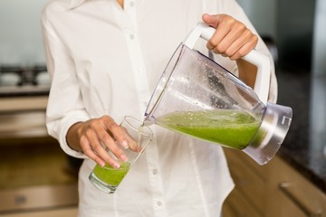 Mid section of woman pouring smoothie in a glass