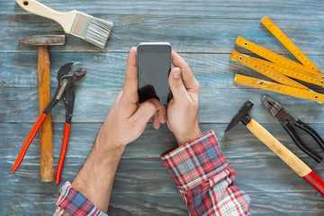 Man working on a DIY project with his phone, wood shavings and c