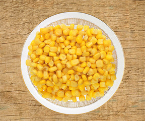 Sweet yellow corn grain on plate on wooden background