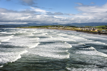 Irland, Rossnowlagh: Panorama Blick auf wunderschöne wilde irische Küste mit Wellen Ozean Meer Stadt Horizont Wolken und blauem Himmel 