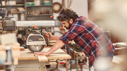 Craftsman using radial arm saw on some wood in workshop