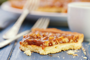 tart with nuts and caramel and cup of coffee on blue background