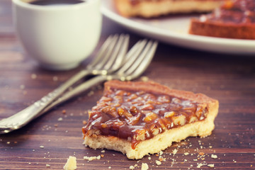 tart with nuts and caramel and cup of coffee on brown wooden background