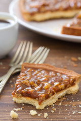 tart with nuts and caramel and cup of coffee on brown background