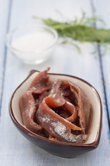 anchovies in dish with salt and herbs on blue wooden background