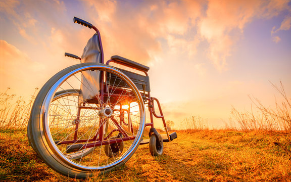 Empty wheelchair on the meadow at sunset