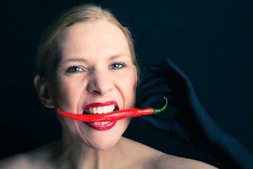 Blonde woman bites into a red chili