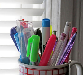 Pens and a small ruler collected in a mug on a desktop.