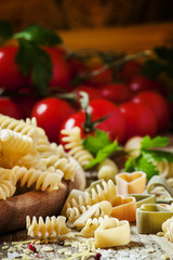 Obraz na płótnie Canvas Italian food: pasta spiraline, herbs, tomatoes on old wooden bac