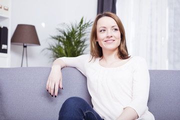 Happy smiling brownd haired young woman sitting on a couch having her arm on the backrest